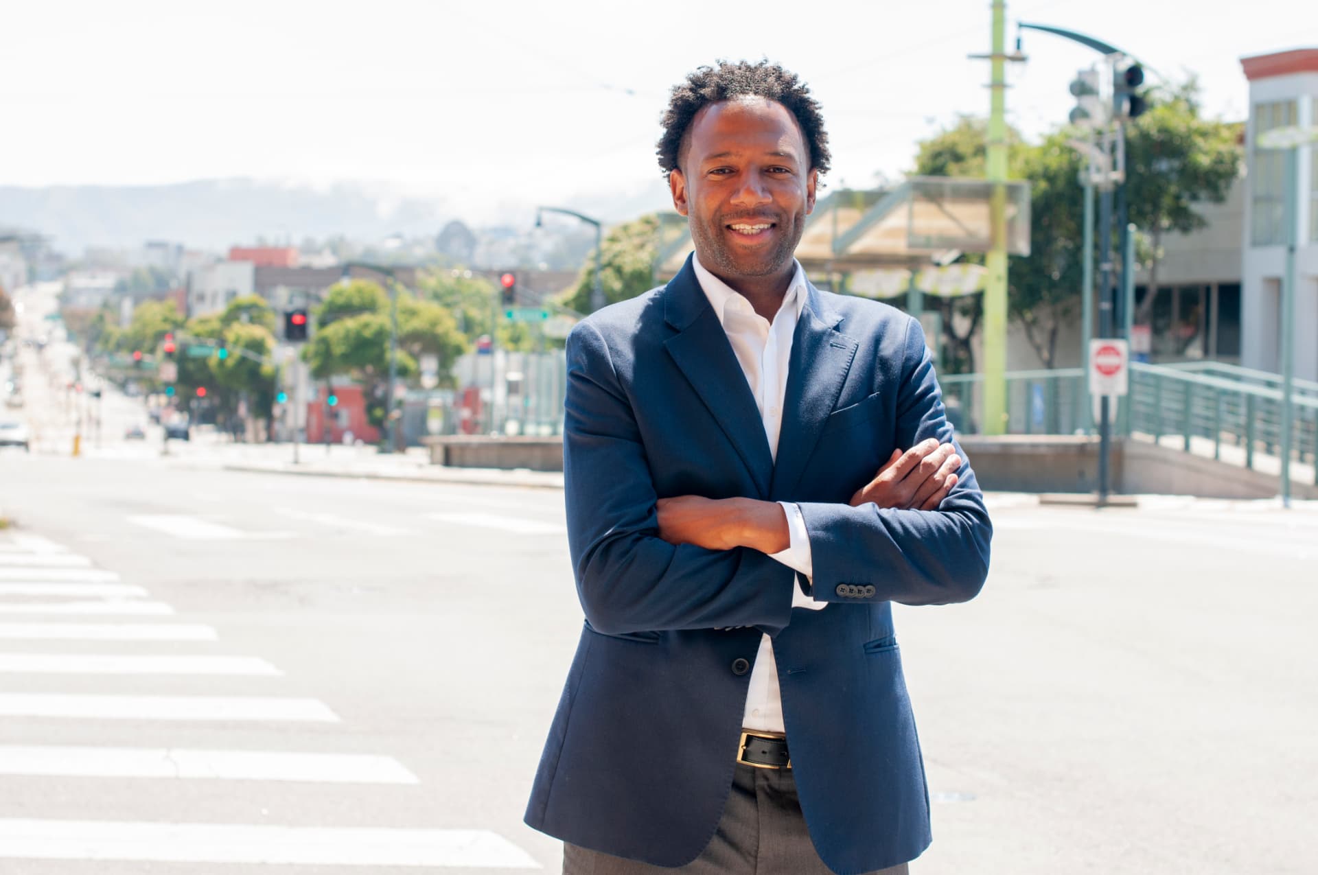 Theo Ellington, candidate for San Francisco District 10 Supervisor, smiling with arms crossed on a sunny District 10 street corner